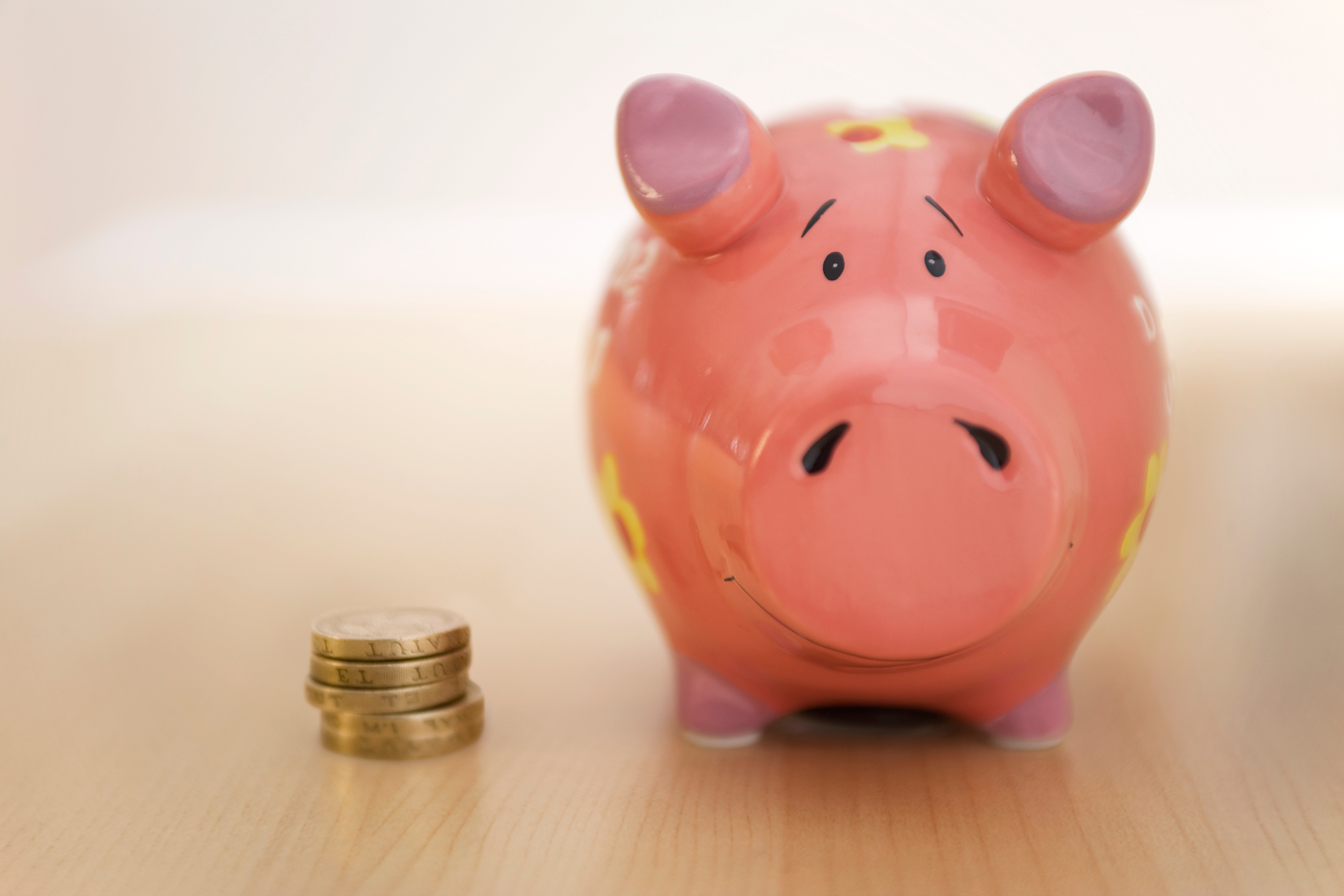 A pink piggy bank and pile of pound coins