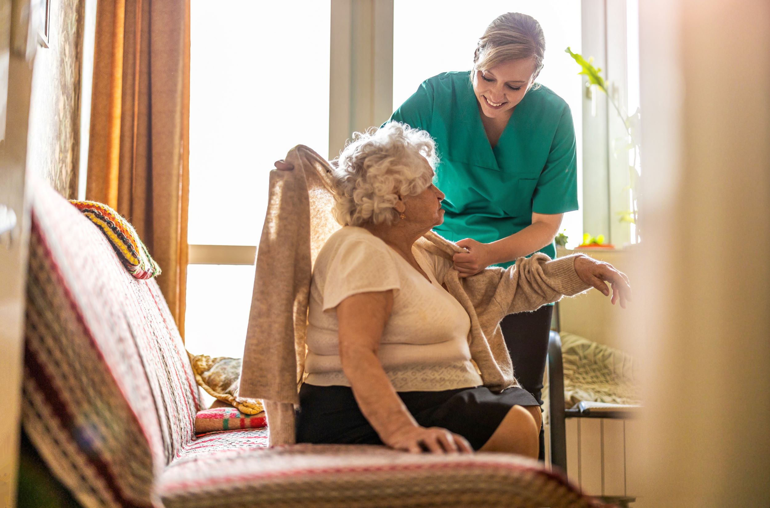 A care worker assisting a woman with her cardigan