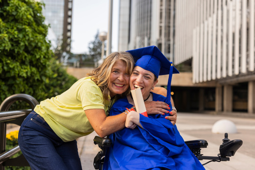 Mother embracing physically disabled young woman at her university graduation